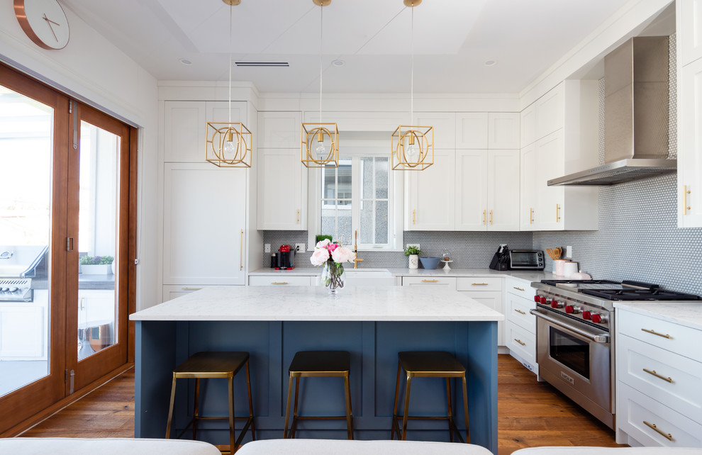 Inspiration for a transitional medium tone wood floor and brown floor kitchen remodel in Vancouver with a farmhouse sink, shaker cabinets, white cabinets, quartz countertops, mosaic tile backsplash, stainless steel appliances, an island and white countertops