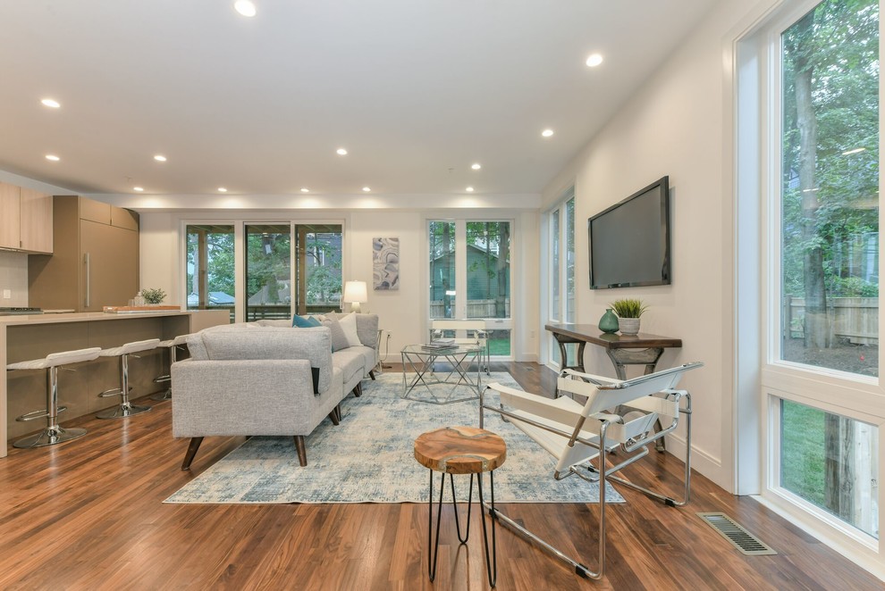 Photo of a large contemporary open concept living room in Boston with white walls, medium hardwood floors, no fireplace, a wall-mounted tv and brown floor.