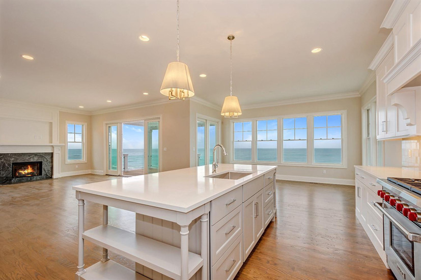 Large beach style single-wall open plan kitchen in Chicago with an undermount sink, shaker cabinets, white cabinets, solid surface benchtops, white splashback, porcelain splashback, stainless steel appliances, light hardwood floors and with island.