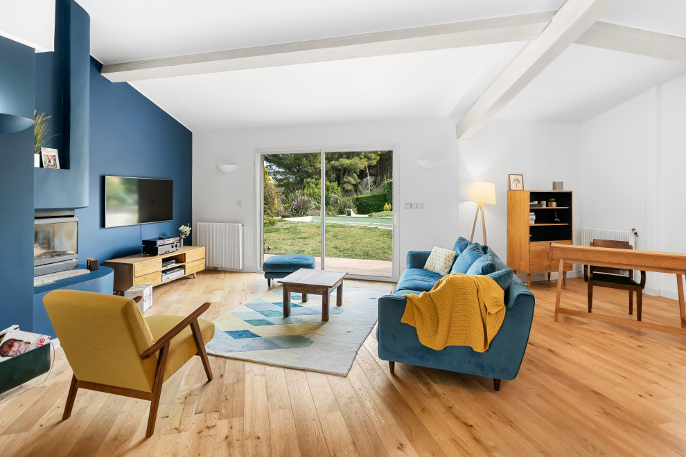 Ispirazione per un grande soggiorno aperto con pareti blu, parquet chiaro, stufa a legna, TV a parete, pavimento beige e travi a vista