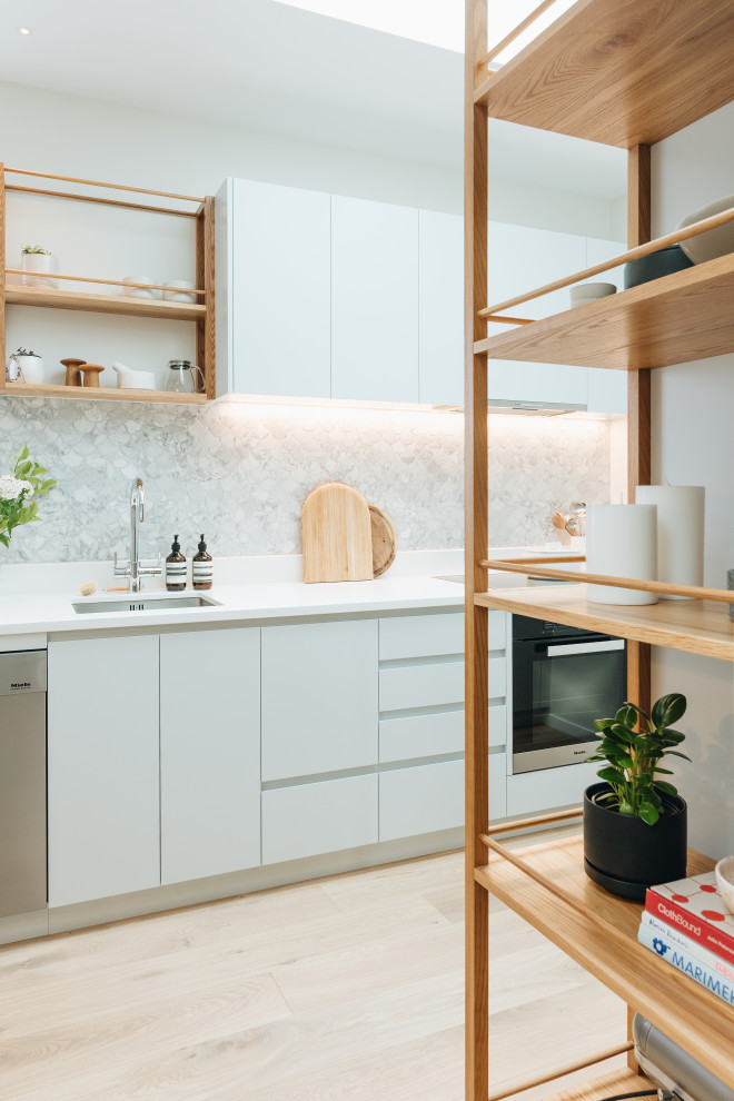 This is an example of a mid-sized contemporary kitchen in Wellington with an undermount sink, green cabinets, quartz benchtops, grey splashback, porcelain splashback, stainless steel appliances, light hardwood floors, no island, brown floor and white benchtop.
