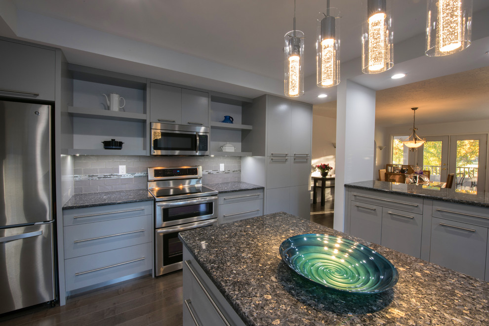 This is an example of a large modern eat-in kitchen in Calgary with a drop-in sink, flat-panel cabinets, grey cabinets, granite benchtops, grey splashback, ceramic splashback, stainless steel appliances, medium hardwood floors and with island.