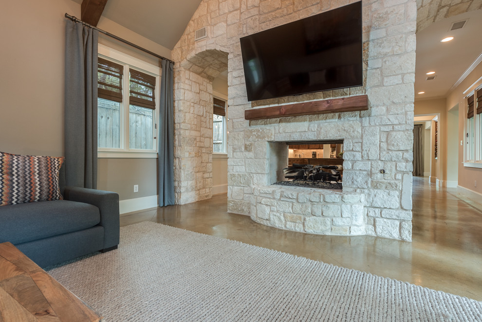 Design ideas for a mid-sized transitional open concept family room in Dallas with concrete floors, a two-sided fireplace, a stone fireplace surround, a wall-mounted tv and beige walls.