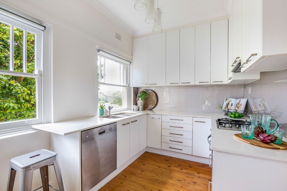 This is an example of a small scandinavian u-shaped kitchen in Sydney with quartz benchtops, grey splashback, glass sheet splashback, stainless steel appliances, light hardwood floors and beige floor.