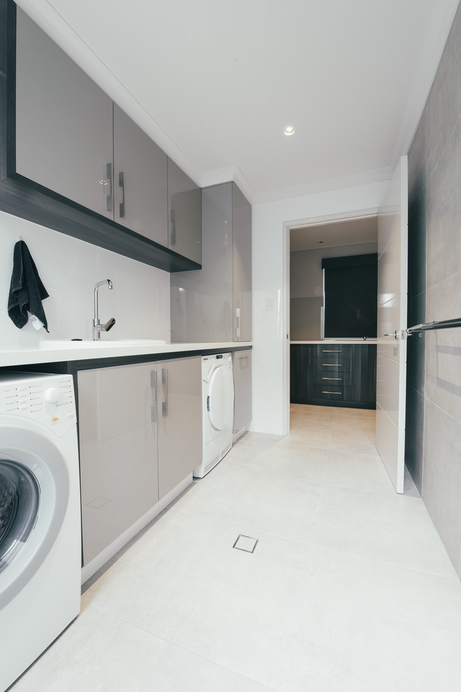 This is an example of a small contemporary single-wall dedicated laundry room in Perth with grey cabinets, quartz benchtops, white walls, ceramic floors, a side-by-side washer and dryer and a drop-in sink.