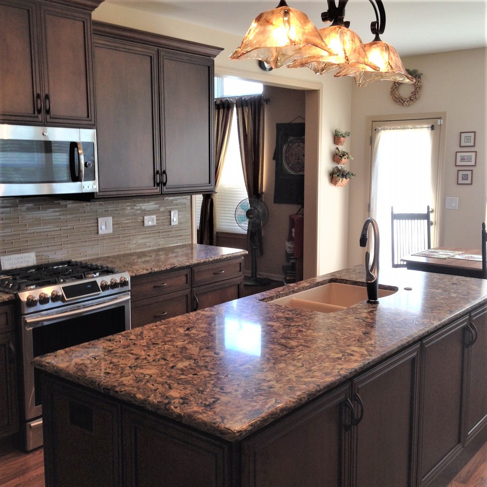 Inspiration for a mid-sized transitional medium tone wood floor and brown floor eat-in kitchen remodel in Chicago with a double-bowl sink, recessed-panel cabinets, brown cabinets, quartz countertops, beige backsplash, glass sheet backsplash, stainless steel appliances and an island