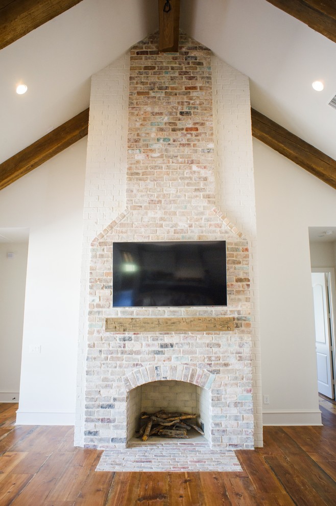 Inspiration for a large traditional open concept family room in Houston with white walls, medium hardwood floors, a standard fireplace, a brick fireplace surround, a wall-mounted tv and brown floor.