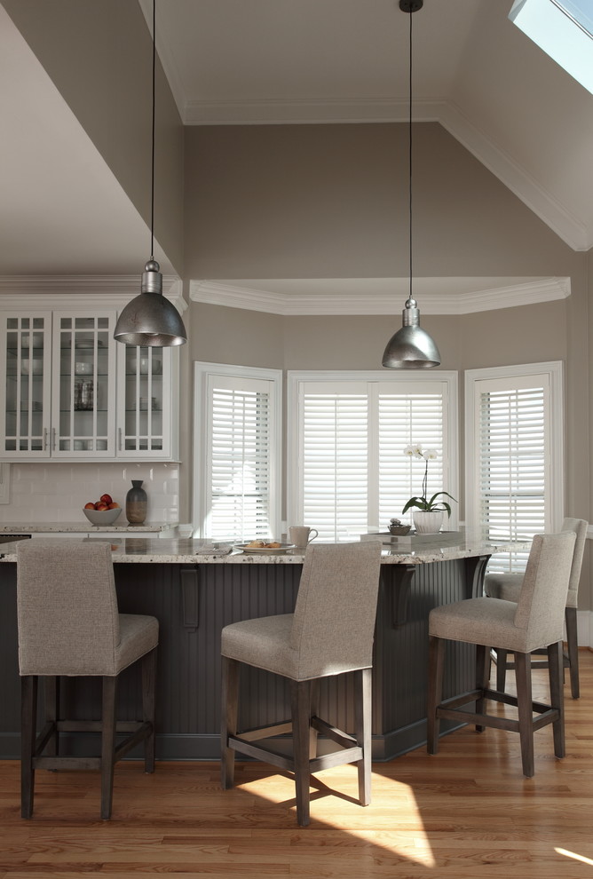 Example of a mid-sized transitional l-shaped light wood floor and beige floor enclosed kitchen design with shaker cabinets, gray cabinets, granite countertops, white backsplash, porcelain backsplash, stainless steel appliances and an island