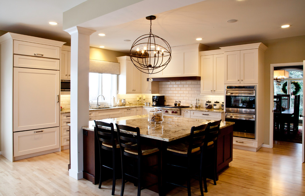 Inspiration for a large transitional l-shaped light wood floor and brown floor open concept kitchen remodel with an undermount sink, shaker cabinets, white cabinets, granite countertops, white backsplash, subway tile backsplash, paneled appliances and an island