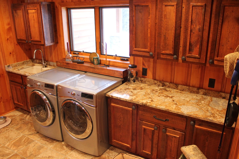 This is an example of a large country single-wall utility room in Other with a single-bowl sink, recessed-panel cabinets, granite benchtops, travertine floors, a side-by-side washer and dryer, dark wood cabinets and brown walls.