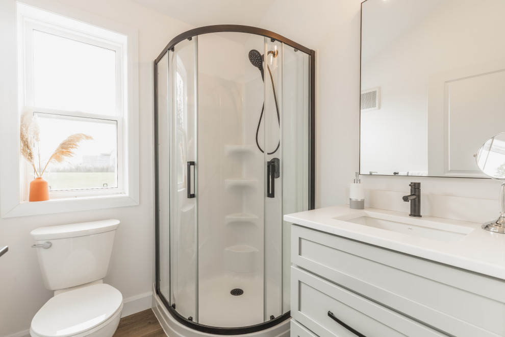 На фото: маленькая ванная комната в стиле модернизм с фасадами с утопленной филенкой, серыми фасадами, угловым душем, унитазом-моноблоком, белыми стенами, полом из винила, душевой кабиной, накладной раковиной, столешницей из искусственного кварца, коричневым полом, душем с раздвижными дверями, белой столешницей, тумбой под одну раковину, встроенной тумбой и сводчатым потолком для на участке и в саду с