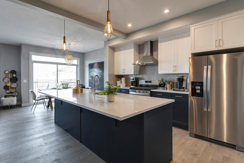 Photo of a modern single-wall eat-in kitchen in Other with an undermount sink, shaker cabinets, blue cabinets, quartzite benchtops, grey splashback, ceramic splashback, stainless steel appliances, light hardwood floors, with island, brown floor and white benchtop.