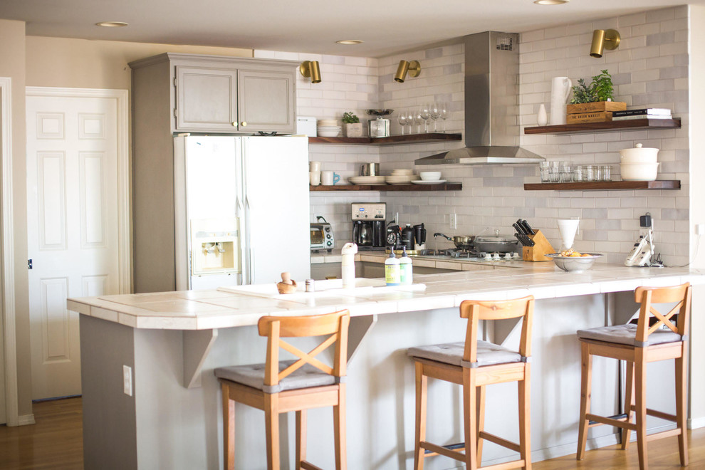 Mid-sized mountain style u-shaped medium tone wood floor and brown floor eat-in kitchen photo in Seattle with a drop-in sink, recessed-panel cabinets, beige cabinets, tile countertops, white backsplash, brick backsplash, white appliances, a peninsula and beige countertops