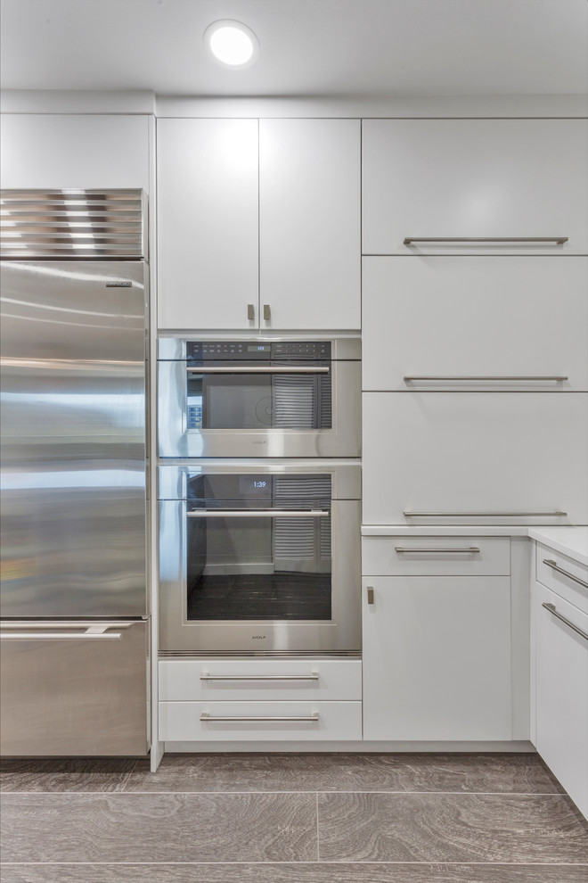 Inspiration for a large contemporary u-shaped separate kitchen in Tampa with an undermount sink, flat-panel cabinets, white cabinets, quartz benchtops, white splashback, ceramic splashback, stainless steel appliances, medium hardwood floors, brown floor and white benchtop.