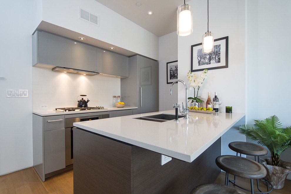 This is an example of a small modern u-shaped eat-in kitchen in New York with a double-bowl sink, flat-panel cabinets, grey cabinets, solid surface benchtops, stainless steel appliances, medium hardwood floors and a peninsula.