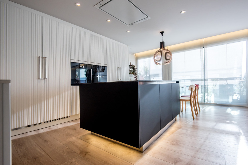 Inspiration for a mid-sized contemporary eat-in kitchen in Barcelona with a double-bowl sink, white cabinets, white splashback, black appliances, with island and brown floor.