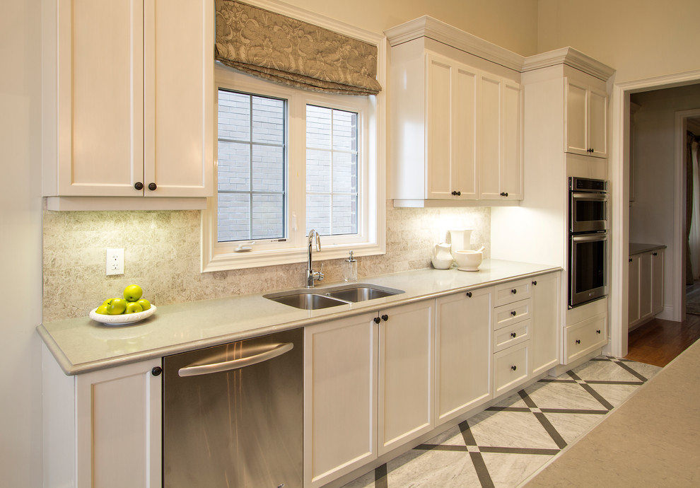 Photo of a large transitional u-shaped eat-in kitchen in Detroit with a double-bowl sink, shaker cabinets, white cabinets, quartz benchtops, beige splashback, travertine splashback, stainless steel appliances, marble floors, with island and white floor.