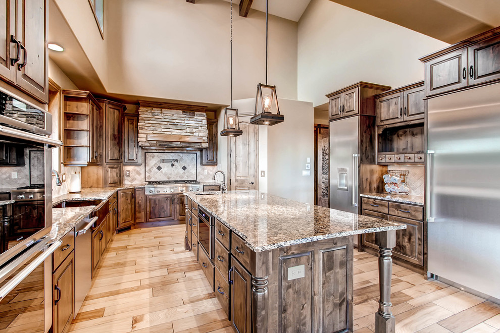 Large country u-shaped kitchen in Denver with a farmhouse sink, raised-panel cabinets, dark wood cabinets, granite benchtops, beige splashback, stone tile splashback, stainless steel appliances, light hardwood floors, with island, brown floor and multi-coloured benchtop.