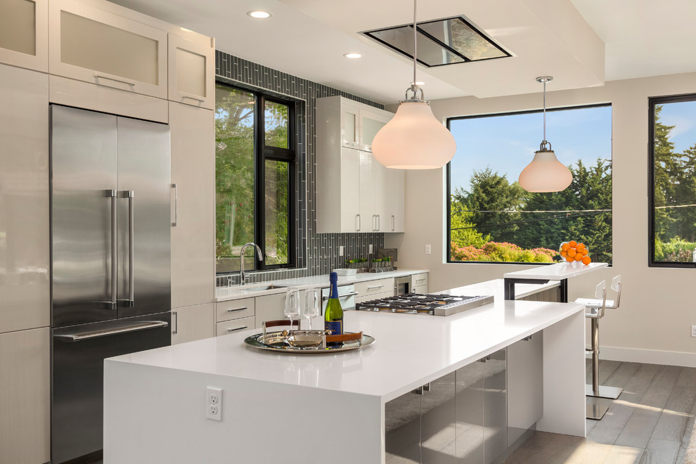Inspiration for a mid-sized contemporary galley medium tone wood floor and brown floor open concept kitchen remodel in Los Angeles with an undermount sink, flat-panel cabinets, white cabinets, solid surface countertops, gray backsplash, matchstick tile backsplash, stainless steel appliances and an island