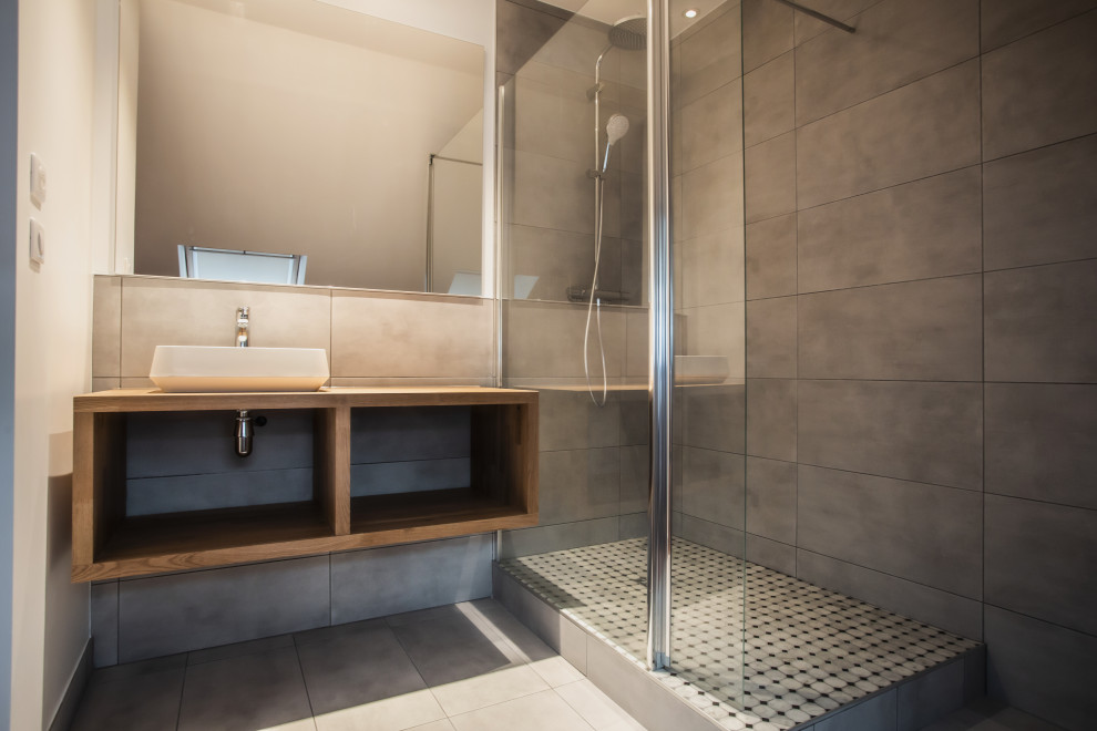 Contemporary 3/4 bathroom in Paris with open cabinets, brown cabinets, an open shower, gray tile, ceramic tile, grey walls, ceramic floors, a trough sink, wood benchtops, grey floor and brown benchtops.