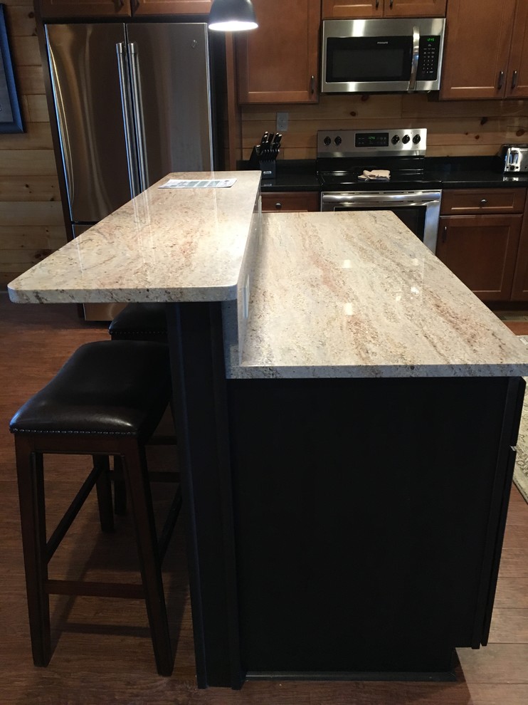 Mountain style l-shaped laminate floor and brown floor eat-in kitchen photo with a double-bowl sink, flat-panel cabinets, dark wood cabinets, granite countertops, black backsplash, stainless steel appliances, an island and black countertops