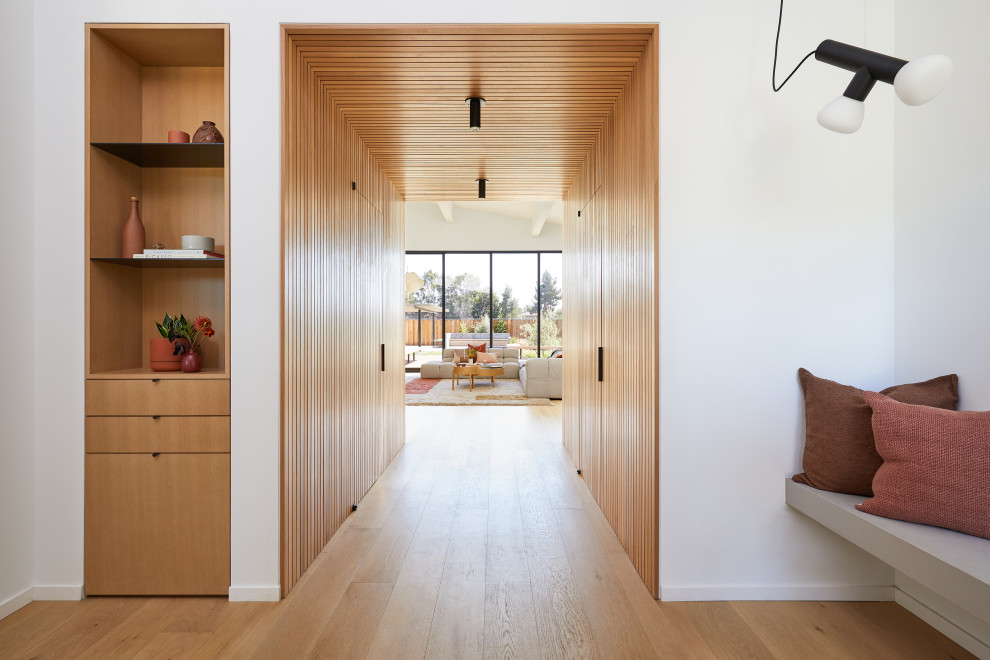 Design ideas for a mid-sized modern foyer in San Francisco with white walls, light hardwood floors, a pivot front door, a light wood front door, brown floor, vaulted and wood walls.