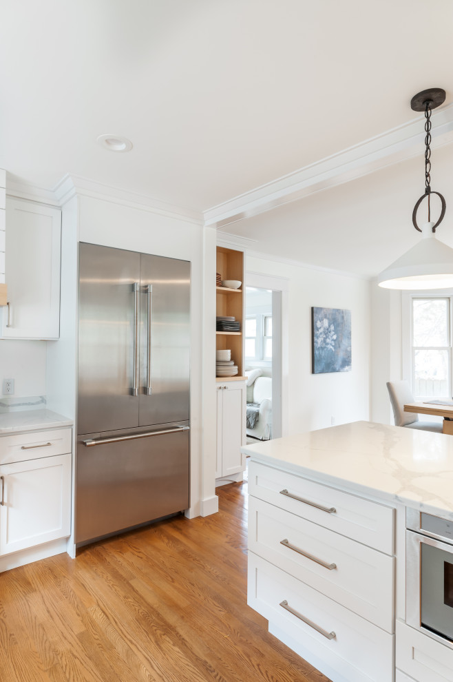 Large transitional l-shaped medium tone wood floor eat-in kitchen photo in Detroit with a farmhouse sink, shaker cabinets, white cabinets, quartz countertops, white backsplash, quartz backsplash, stainless steel appliances, an island and white countertops