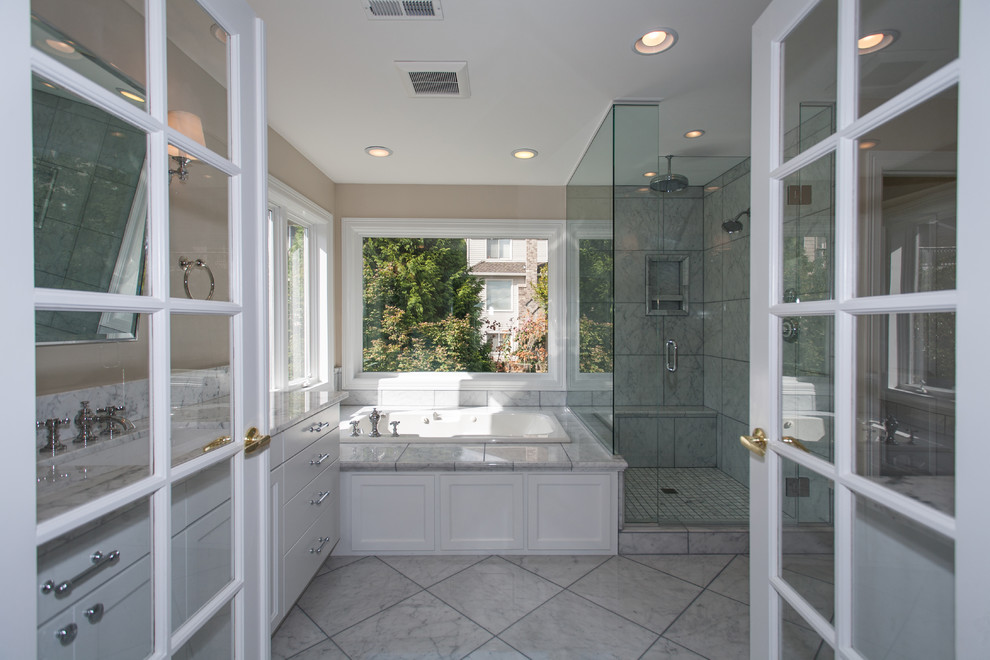 Photo of a mid-sized transitional master bathroom in Portland with shaker cabinets, white cabinets, a drop-in tub, a corner shower, gray tile, white tile, marble, beige walls, marble floors, an undermount sink, marble benchtops, grey floor, a hinged shower door and grey benchtops.