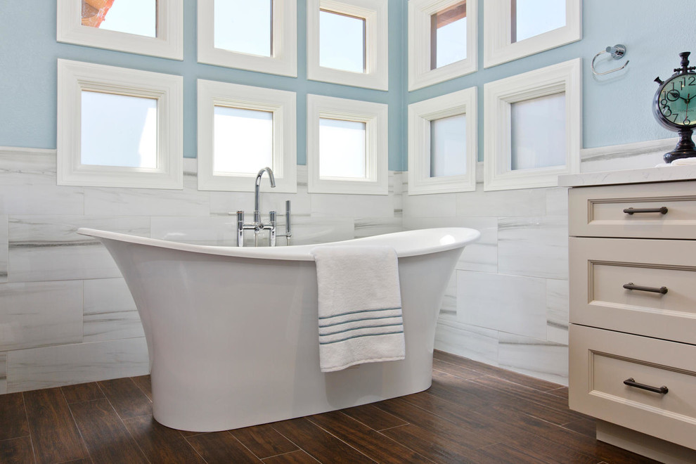 Photo of a large traditional master bathroom in Denver with recessed-panel cabinets, white cabinets, a freestanding tub, an open shower, a wall-mount toilet, yellow tile, porcelain tile, blue walls, porcelain floors, an undermount sink and engineered quartz benchtops.