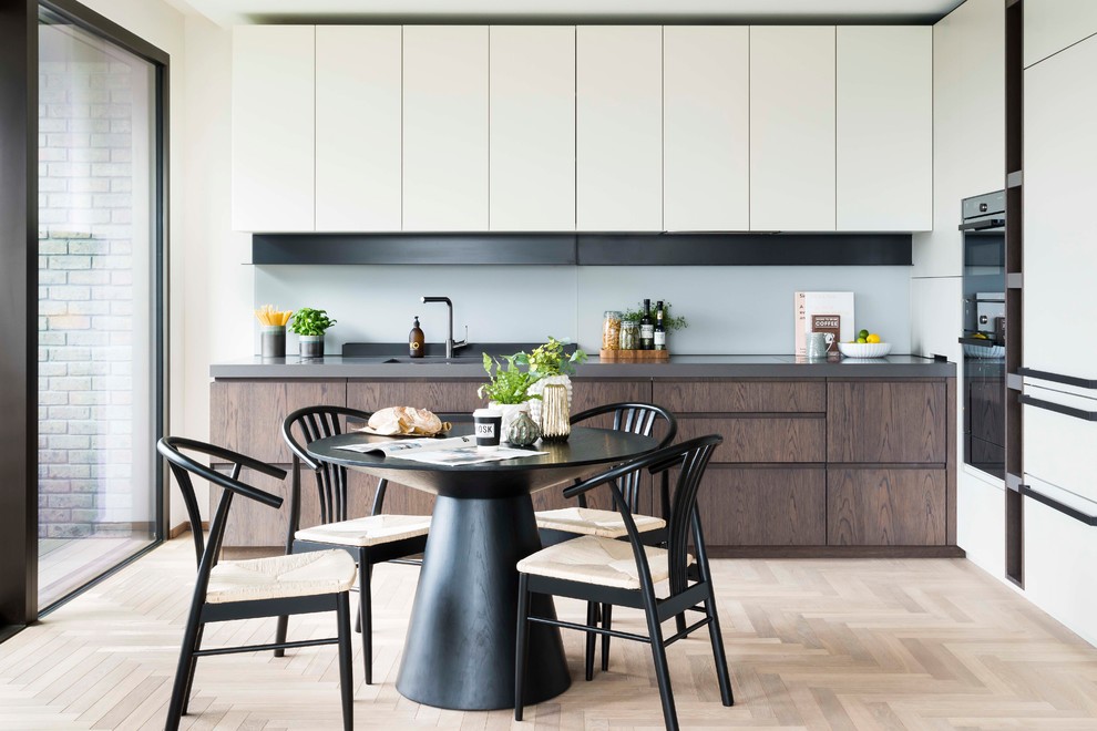 Inspiration for a contemporary l-shaped eat-in kitchen in London with flat-panel cabinets, white cabinets, stainless steel appliances, light hardwood floors, no island, beige floor and grey benchtop.