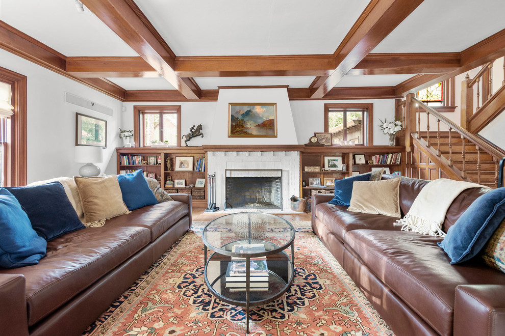 This is an example of a traditional open concept living room in Raleigh with a library, white walls, medium hardwood floors, a standard fireplace, a brick fireplace surround and no tv.