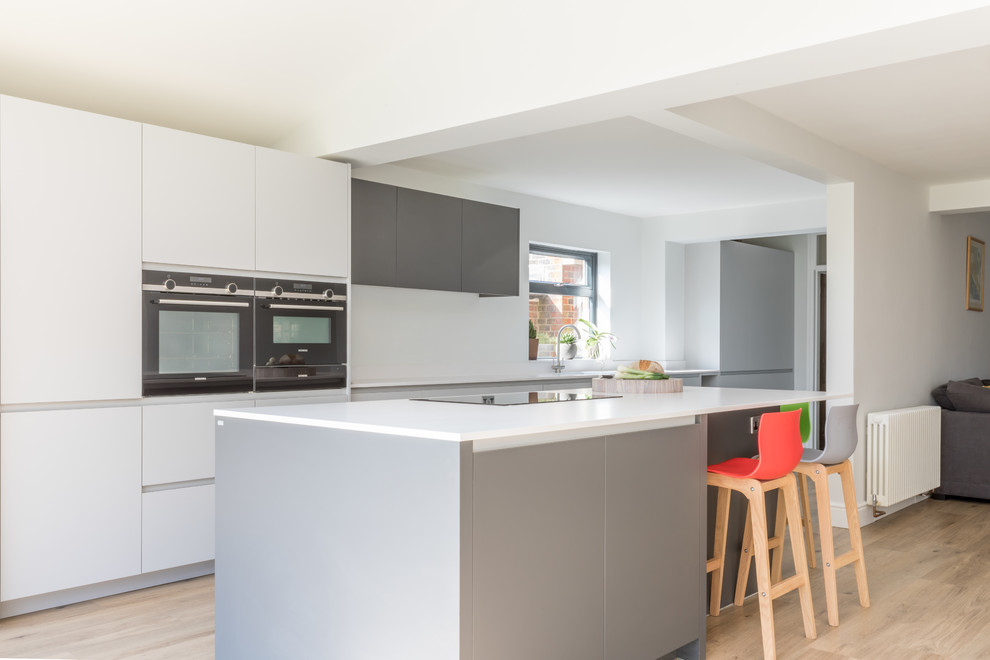 Photo of a mid-sized contemporary galley open plan kitchen in Sussex with an integrated sink, flat-panel cabinets, grey cabinets, solid surface benchtops, stainless steel appliances, with island and white benchtop.