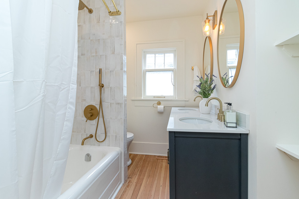 Example of a small transitional white tile medium tone wood floor, beige floor and double-sink drop-in bathtub design with shaker cabinets, blue cabinets, a two-piece toilet, white walls, an undermount sink, soapstone countertops, white countertops and a freestanding vanity