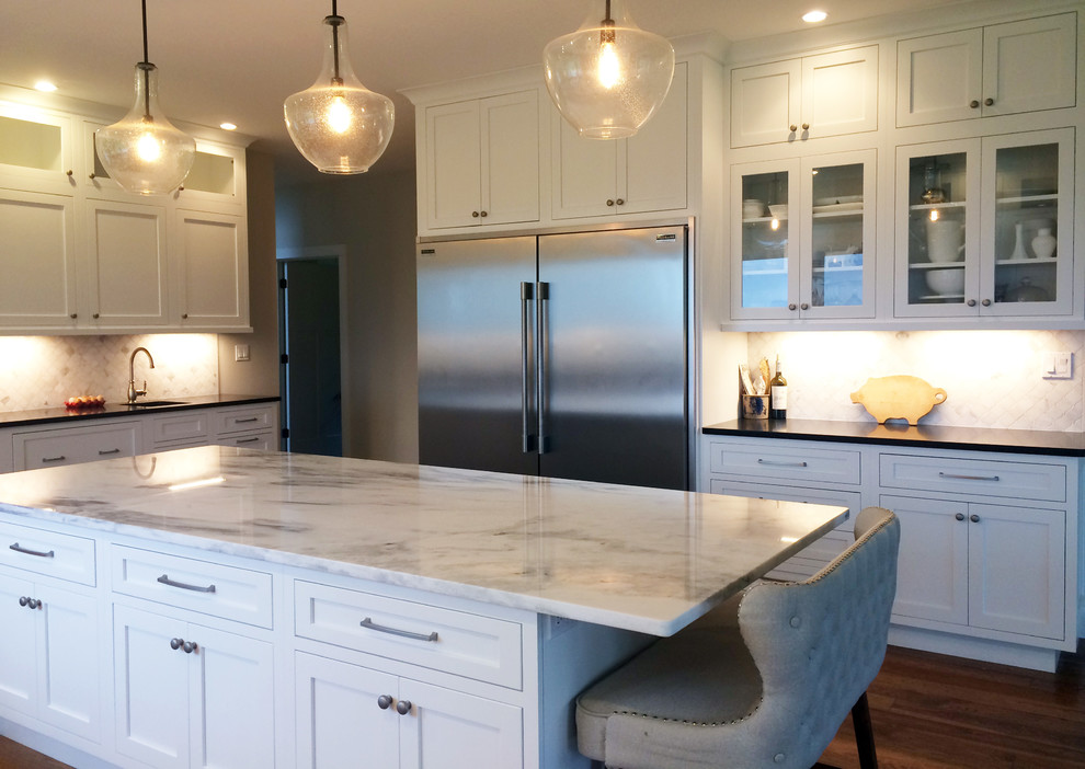 Large transitional u-shaped kitchen pantry photo with a farmhouse sink, recessed-panel cabinets, white cabinets, quartzite countertops, stainless steel appliances, an island and black countertops