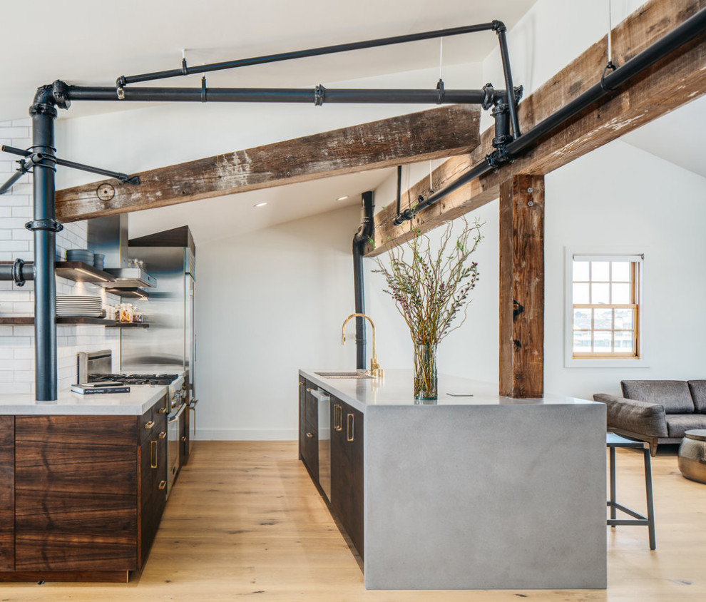 Photo of a mid-sized industrial l-shaped open plan kitchen in San Francisco with dark wood cabinets, white splashback, brick splashback, stainless steel appliances, light hardwood floors, with island and grey benchtop.