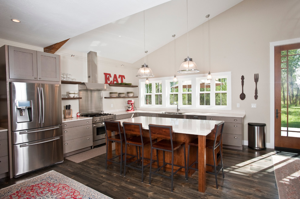 Large transitional l-shaped dark wood floor and brown floor open concept kitchen photo with a farmhouse sink, flat-panel cabinets, gray cabinets, quartz countertops, stainless steel appliances and an island