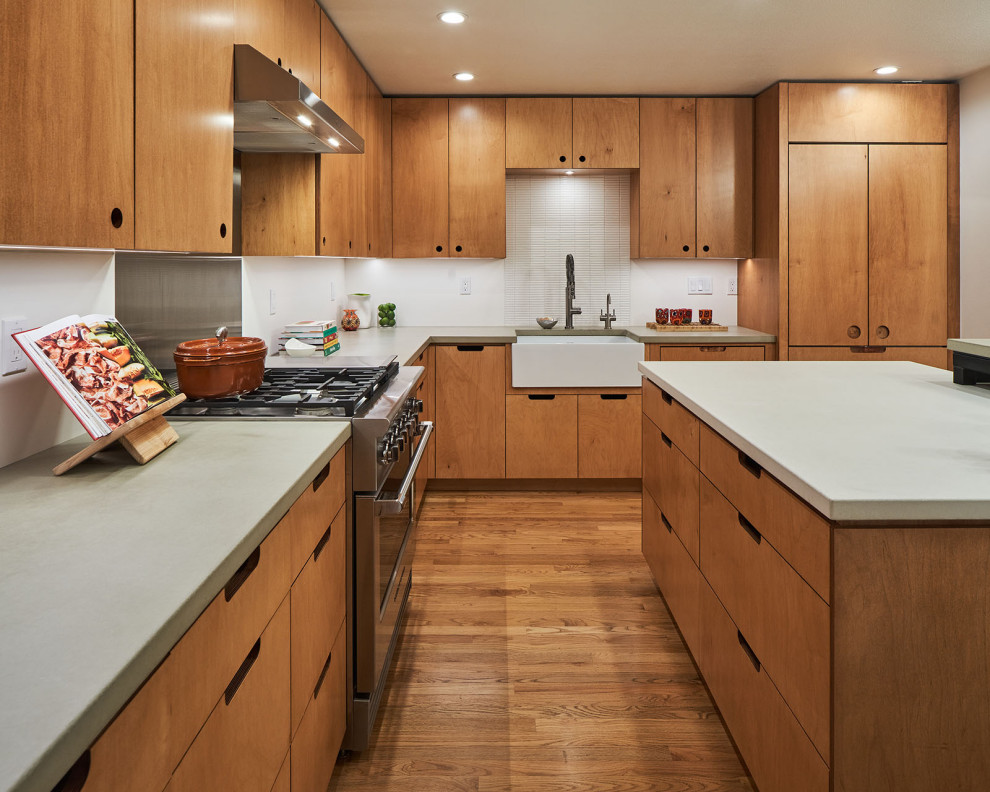 Small contemporary l-shaped kitchen/diner in Portland with a belfast sink, flat-panel cabinets, medium wood cabinets, concrete worktops, white splashback, integrated appliances, medium hardwood flooring, an island and grey worktops.