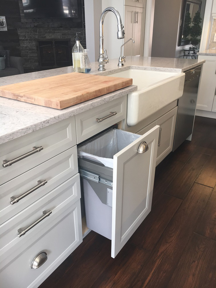 Example of a transitional l-shaped brown floor eat-in kitchen design with a farmhouse sink, white cabinets, quartz countertops, stainless steel appliances, an island and white countertops