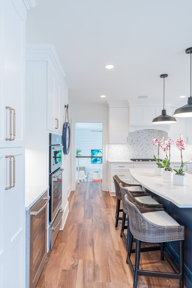 This is an example of a large beach style u-shaped eat-in kitchen in Philadelphia with an undermount sink, shaker cabinets, white cabinets, quartz benchtops, white splashback, marble splashback, panelled appliances, vinyl floors, with island, brown floor and white benchtop.