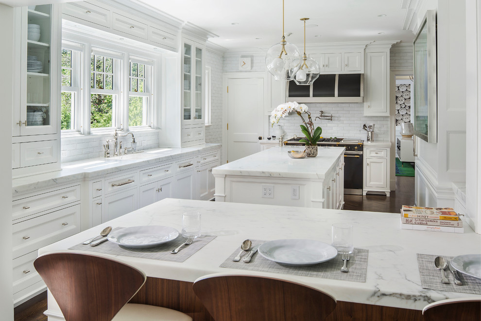 Inspiration for a large traditional l-shaped eat-in kitchen in New York with recessed-panel cabinets, white cabinets, white splashback, black appliances, dark hardwood floors, with island, a single-bowl sink, marble benchtops and subway tile splashback.