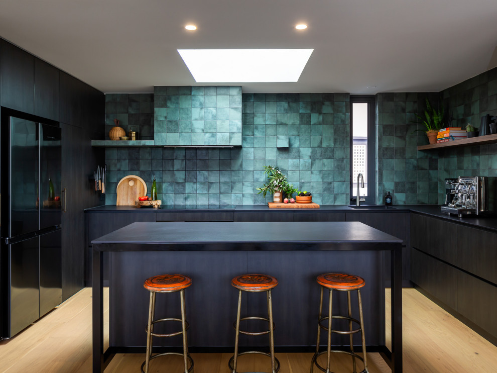 Inspiration for a contemporary u-shaped kitchen in Adelaide with an undermount sink, flat-panel cabinets, black cabinets, green splashback, black appliances, light hardwood floors, with island, beige floor and black benchtop.