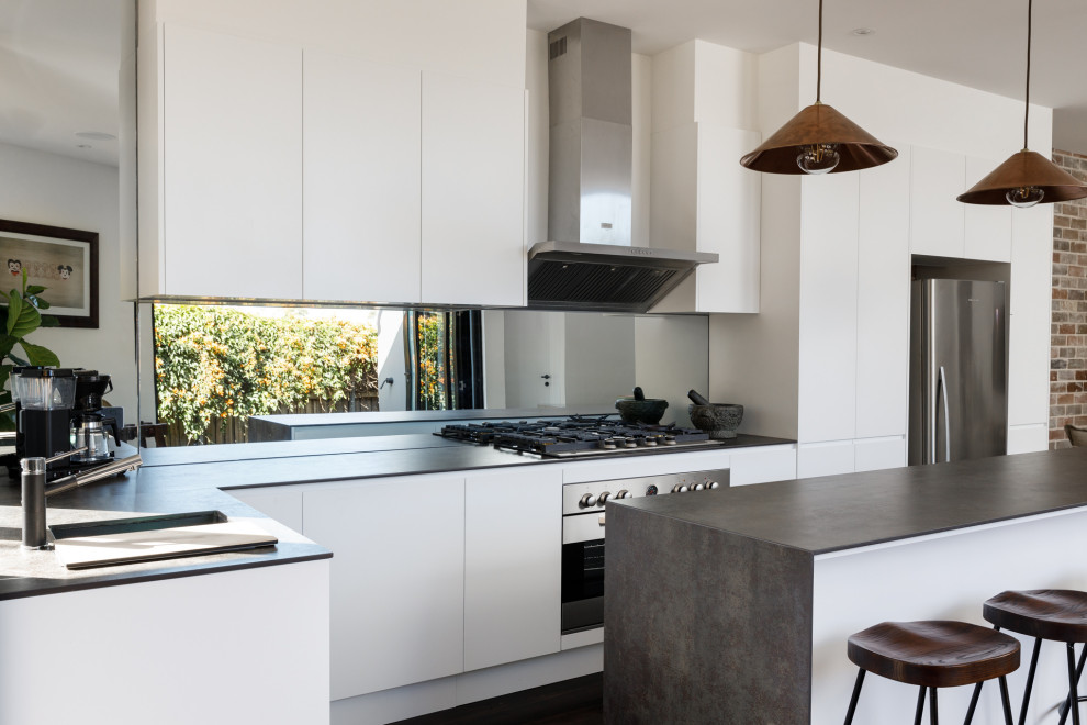 Design ideas for a contemporary galley open plan kitchen in Sydney with a drop-in sink, white cabinets, solid surface benchtops, mirror splashback, stainless steel appliances, painted wood floors, with island, black floor and grey benchtop.