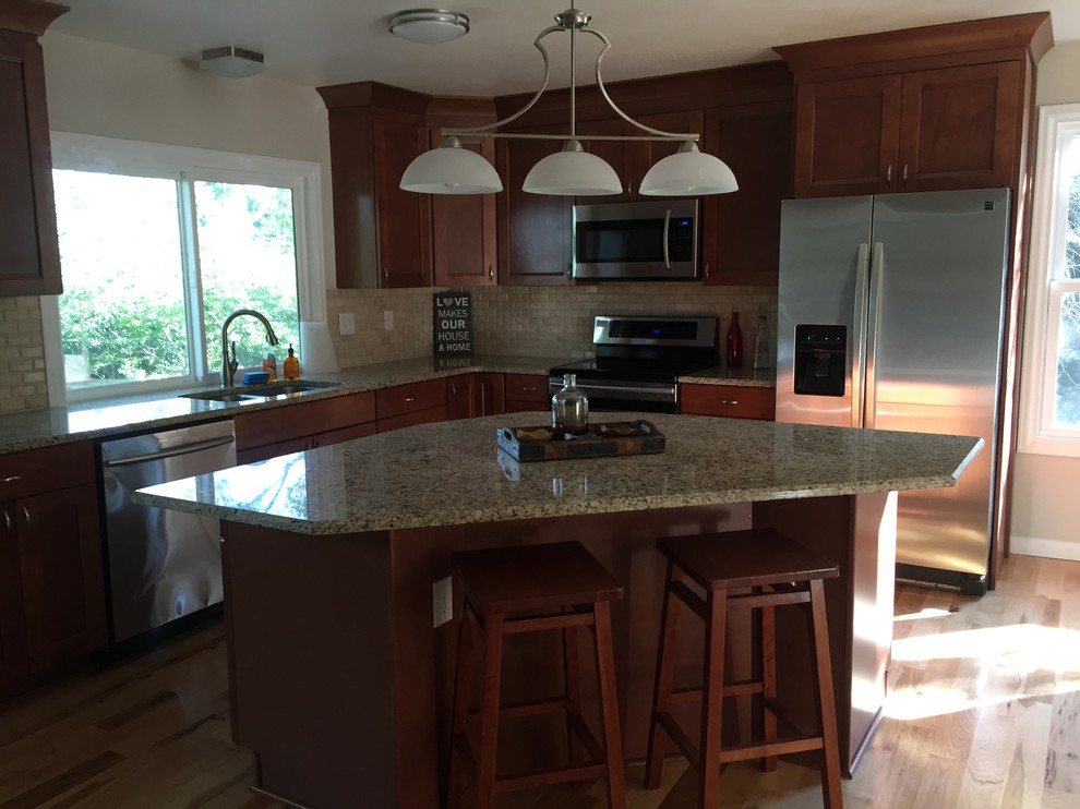 Open concept kitchen - transitional l-shaped light wood floor open concept kitchen idea in Denver with an undermount sink, shaker cabinets, medium tone wood cabinets, granite countertops, beige backsplash, stone tile backsplash, stainless steel appliances and an island