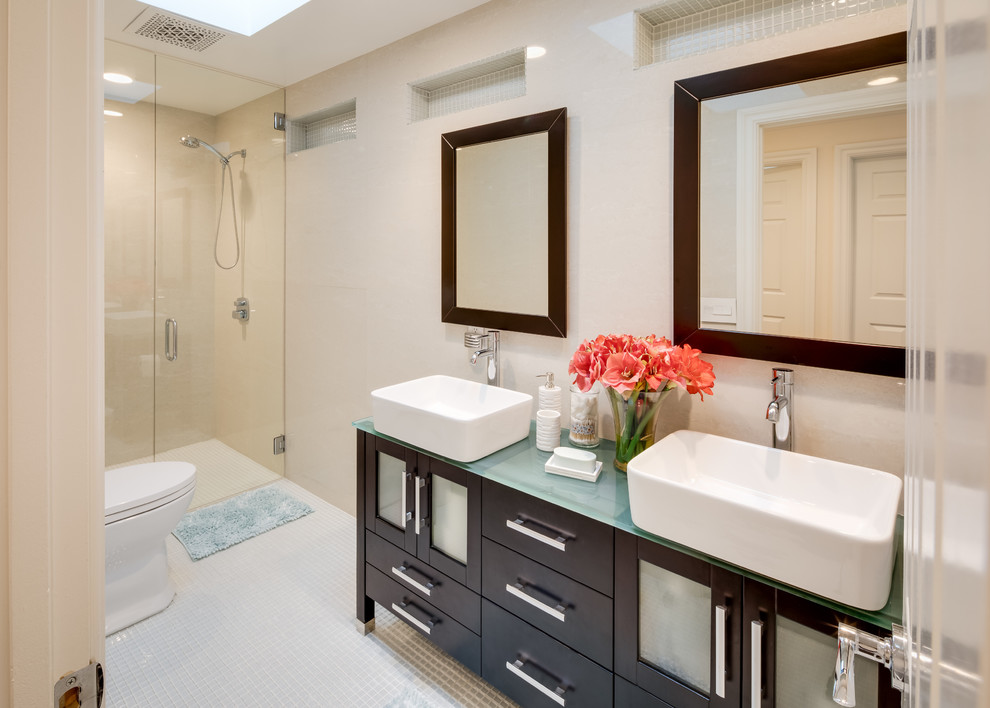 This is an example of a mid-sized traditional 3/4 bathroom in San Diego with dark wood cabinets, a curbless shower, a two-piece toilet, beige walls, mosaic tile floors, a vessel sink, glass benchtops, beige floor, a hinged shower door and shaker cabinets.