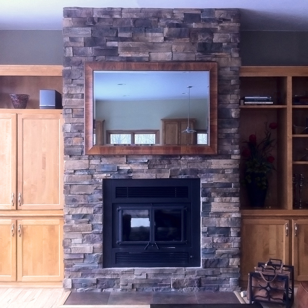Photo of a mid-sized enclosed living room in Other with a library, brown walls, a standard fireplace, a stone fireplace surround, a concealed tv and brown floor.
