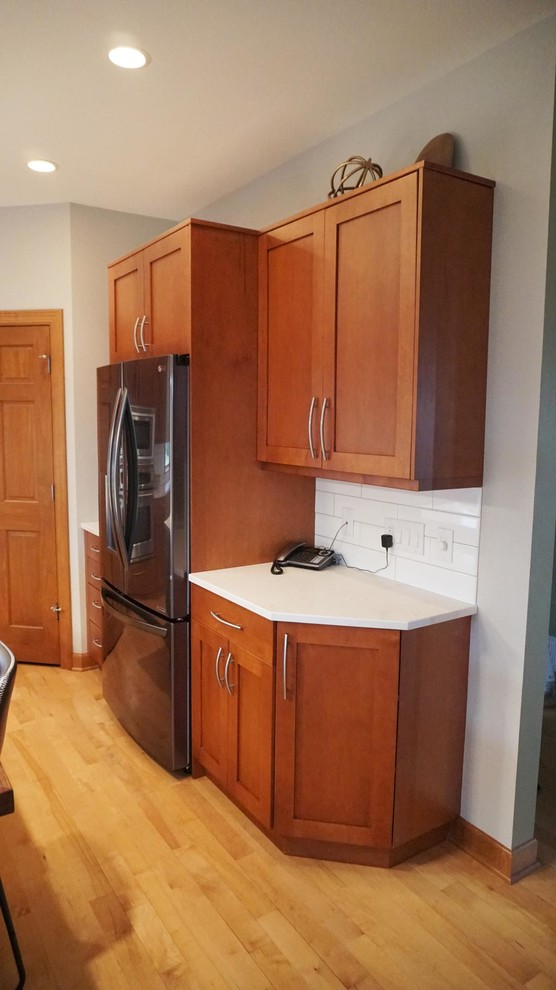 Inspiration for a large transitional l-shaped medium tone wood floor open concept kitchen remodel with an undermount sink, recessed-panel cabinets, brown cabinets, white backsplash, subway tile backsplash, stainless steel appliances, an island and white countertops