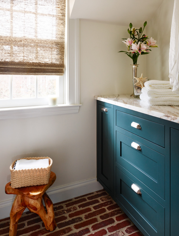 This is an example of a small traditional galley dedicated laundry room in Boston with an utility sink, shaker cabinets, green cabinets, marble benchtops, white splashback, white walls, brick floors, a stacked washer and dryer, red floor, white benchtop and planked wall panelling.