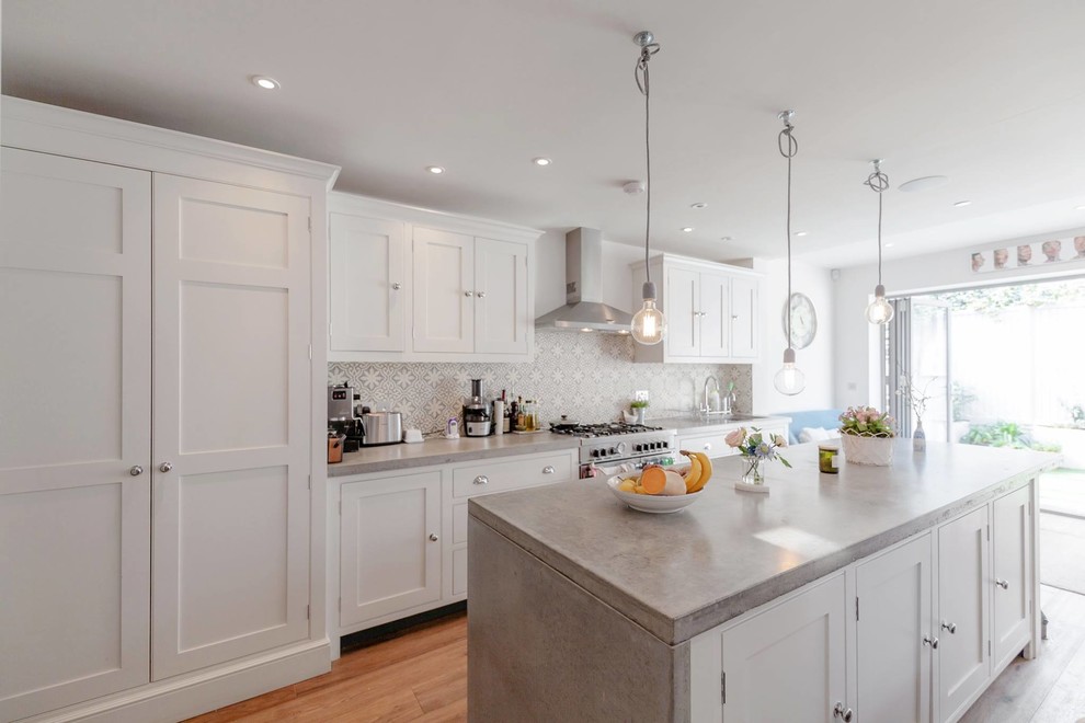 This is an example of a mid-sized contemporary single-wall separate kitchen in London with with island, shaker cabinets, white cabinets, concrete benchtops, cement tile splashback, white appliances, medium hardwood floors and brown floor.