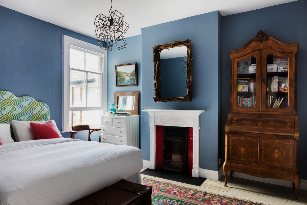 Design ideas for a mid-sized traditional guest bedroom in London with blue walls, light hardwood floors, a standard fireplace and a wood fireplace surround.
