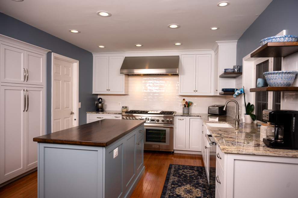 ワシントンD.C.にある高級な中くらいなカントリー風のおしゃれなキッチン (エプロンフロントシンク、シェーカースタイル扉のキャビネット、青いキャビネット、御影石カウンター、白いキッチンパネル、サブウェイタイルのキッチンパネル、シルバーの調理設備、淡色無垢フローリング、黄色い床、マルチカラーのキッチンカウンター) の写真